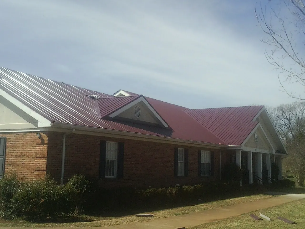 Red metal roof with gabled entries on a long brick building, from a Hail Damage Roof Repair job in Payson